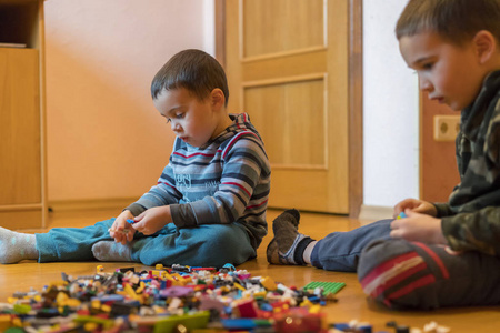 两个孩子在室内的地板上玩着许多五颜六色的塑料块。 两个弟弟扮演建设者。 交流和友谊