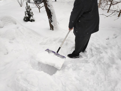 人们用铲子从小路上清除雪，冬天的雪天背景。 在大雪中，人们在车道上铲雪。 特写构图