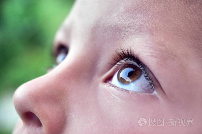 闭上一只小女孩(孩子)的眼睛仰望天空,背景是一个花园.