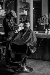 时髦的客户得到理发。理发剪修剪的头发在客户的寺庙。理发师与理发剪工作的发型胡子男子理发店背景。时髦的生活方式概念