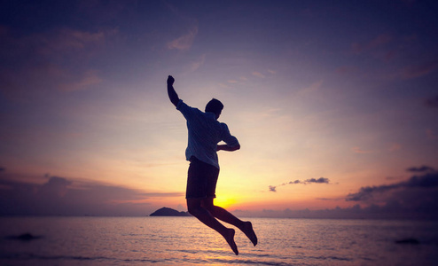 日落时海边一个跳跃的男人的剪影，男人和自然的概念，美丽的生活方式，自由度假旅行