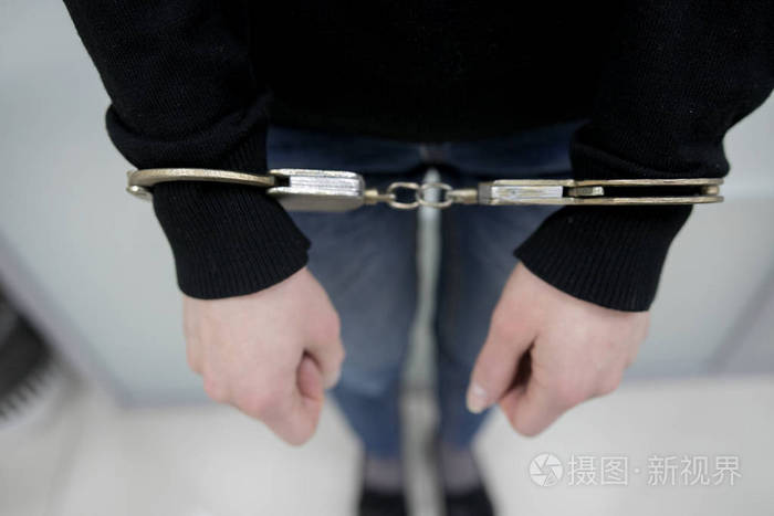 被捕的人把双手铐在灰色背景上的背部. 囚犯或被逮捕的手被铐住.