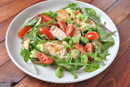 鸡沙拉与鳄梨和樱桃西红柿，胡瓜和甜菜叶。 健康的午餐碗，蔬菜和鸡肉在木制背景上。 健康食品概念