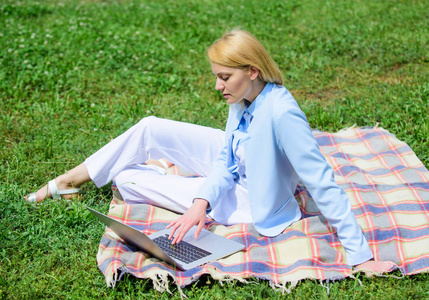 商务野餐的概念。拿着笔记本电脑或笔记本电脑的女人坐在地毯上的绿草草地上。开始自由职业的步骤。商务女士自由职业者在户外工作。在线经
