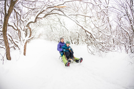 母亲带着一个孩子骑在雪橇上。 一个女人和她的儿子坐着雪橇下山。 这个男孩花时间和他的父母在一起。 有趣的寒假。