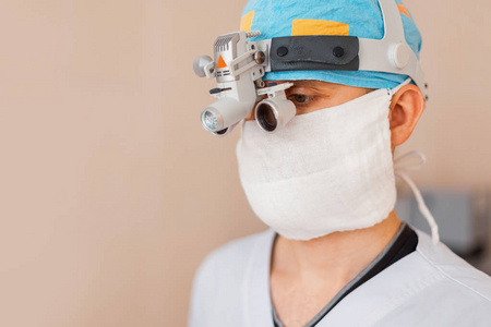 年轻的外科医生穿着一件白色的外套，带着专业的放大镜和二元百叶窗，用于显微外科手术。 现代化设备的外科手术