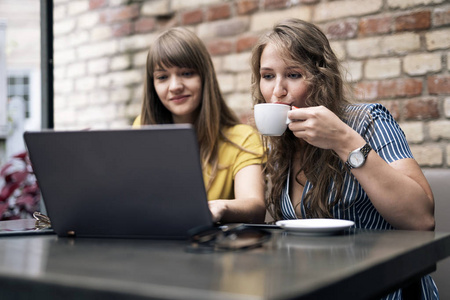 时尚的年轻女性在使用笔记本电脑时与咖啡杯进行友好的会面