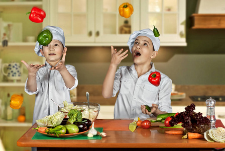 穿着厨师服装的男孩在厨房切沙拉。 孩子们准备健康的食物。 厨师的友好合作。 摆弄蔬菜。