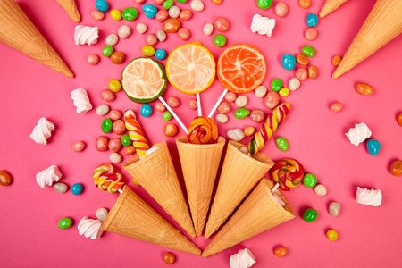 冰淇淋华夫饼锥与彩色糖果糖果果冻棒棒糖在棍子散射多色糖果在粉红色背景。 平躺顶部视图。 复制空间。