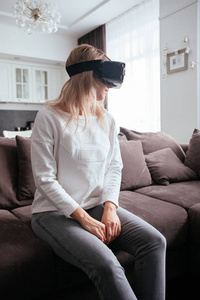 一个年轻的金发女郎在家，带着现代设计，戴上虚拟现实眼镜