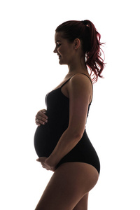 一个怀孕的年轻女孩的颜色剪影。抱着肚子, 微笑着