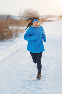 穿着蓝色夹克跑运动女人。 冬天在雪地里慢跑