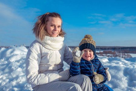 妈妈带着3岁的小儿子, 在阳光明媚的日子里在一个城市里过冬。玩雪球。快乐的微笑放松在大自然中。在清新的空气中快乐的家庭