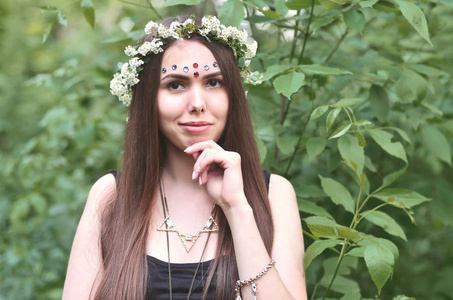 一个情绪化的年轻女孩的肖像，头上戴着花圈，额头上戴着闪亮的装饰品。 一个美丽的白天，在一片欣欣向荣的美丽森林里摆着一个可爱的黑发