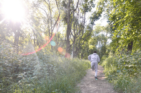 一个穿灰色运动服的年轻人沿着树林里的小路跑。 户外运动