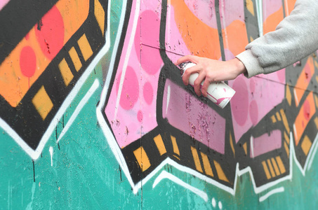 一个穿灰色连帽衫的年轻人的手在雨天的墙上画着粉红色和绿色的涂鸦