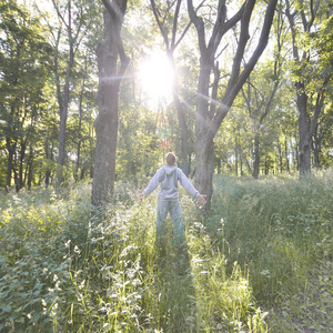 一个穿灰色运动服的年轻人在森林中的树木中享受着太阳的升起。在露天森林里进行体育运动期间的娱乐活动。美丽黎明的喜悦