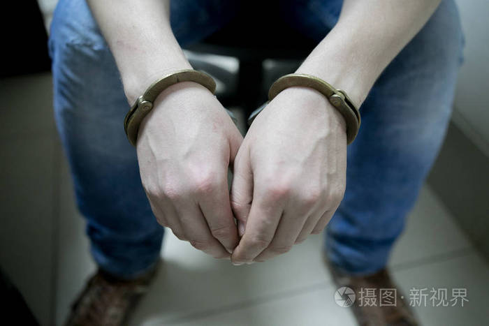 被捕的人把双手铐在灰色背景上的背部.