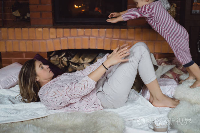 有孩子的年轻女人 妈妈和儿子在壁炉附近玩得很开心.