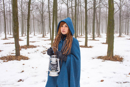 穿着复古蓝色外套的年轻女人在冬天的雾中公园散步，雪和树背景，幻想或仙女的概念