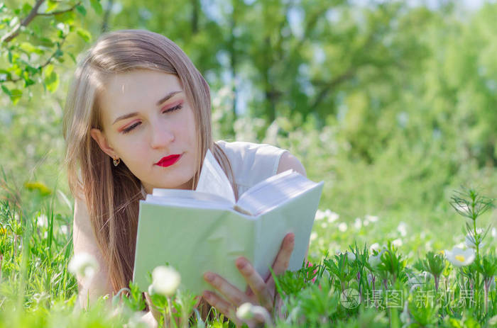 年轻漂亮的女人,白色的顶部,长发躺在草地上,周围是苹果树花园里的花