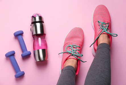 年轻运动的女人的腿哑铃和一瓶水的颜色背景