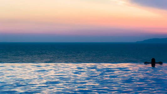 无限游泳池，有黄昏的天空和海洋背景，是放松的好时机。
