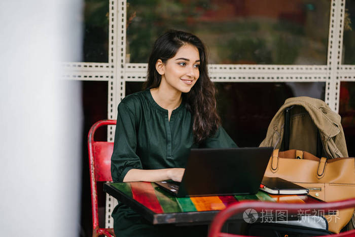年轻的大学生(印度亚裔女性)白天在餐桌上学习和工作她的笔记本电脑