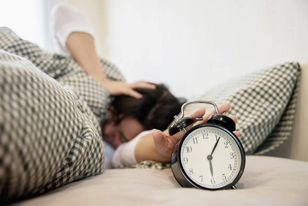 昏昏欲睡的女人早上拿着闹钟，晚醒每天在家生活的概念