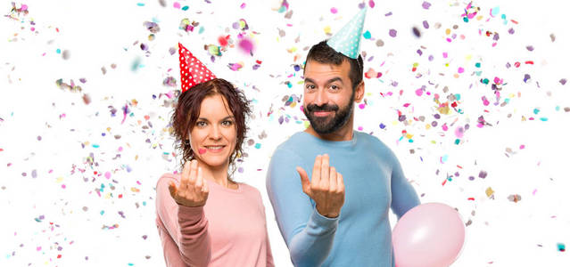 一对夫妇带着气球和生日帽，在聚会上带着五彩纸屑出席和邀请