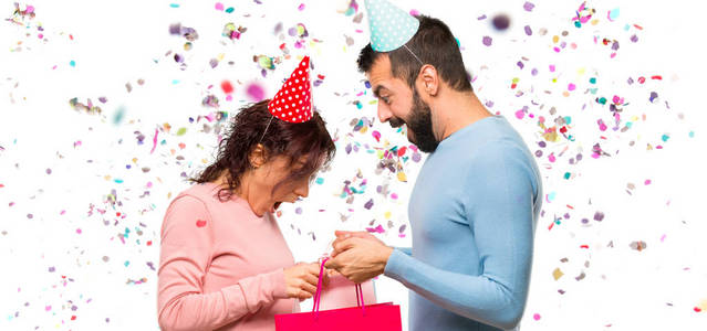 一对夫妇戴着生日帽，带着购物袋和纸屑参加聚会