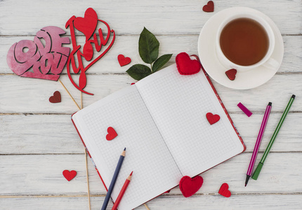 情人节。 笔记本在一张白色的木制桌子上，上面有红色的心。 情人节的浪漫早晨。 顶部视图