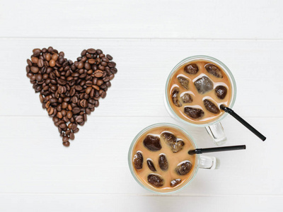 两杯冰咖啡和鸡尾酒管在咖啡豆心脏的背景上。 咖啡豆和牛奶的提神和提神饮料。 从顶部的视图。 平躺着。