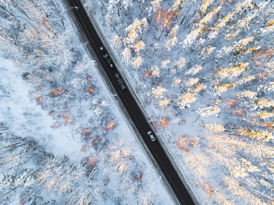 森林冬季道路上汽车的鸟瞰图。 冬季景观乡村。 空中摄影雪林与一辆汽车在路上。 用无人机从上面捕获。 空中照片。 汽车在运动