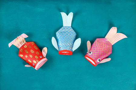 蓝绿色背景下的DIY锦鲤鱼。 中国新年的礼物创意装饰。 孩子是手工制作的。 鲤鱼锦鲤鱼的纸厕所卷Googly眼睛。 一步一步。 
