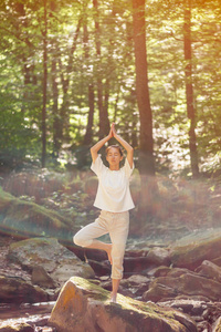 一位闭着眼睛的年轻女子在户外森林里做着树上石上瑜伽。