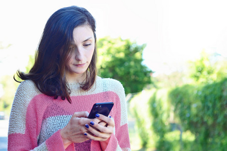 漂亮的年轻女人在街上用智能手机发送信息。