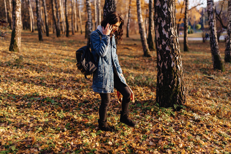 穿牛仔外套的年轻漂亮女孩在秋天阳光明媚的公园散步