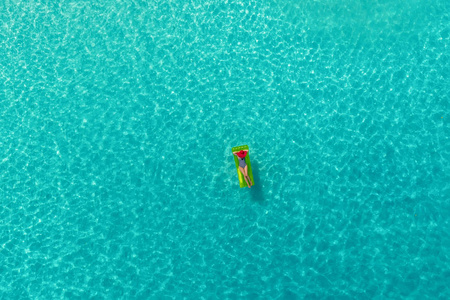 鸟瞰苗条的女人在塞舌尔透明的绿松石海的游泳床垫上游泳。 夏天海景与女孩美丽的波浪，五颜六色的水。 无人驾驶飞机的俯视图