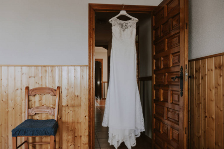 一件白色婚纱挂在木门上，还有一个乡村房子里的椅子