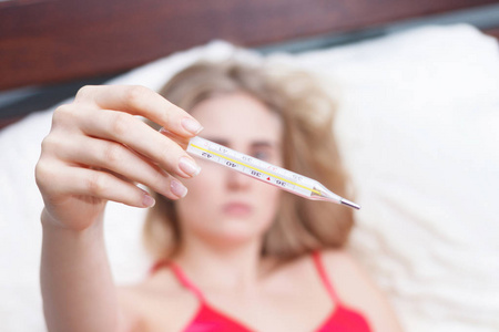 有流感病毒的女人躺在床上，她正在用温度计测量体温