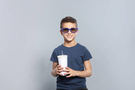 灰色背景电影放映期间带3D眼镜和饮料的男孩