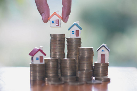 人手把房子模型放在硬币堆叠上，计划储蓄硬币，购买房屋概念抵押贷款和房地产投资。 为房子储蓄或投资。