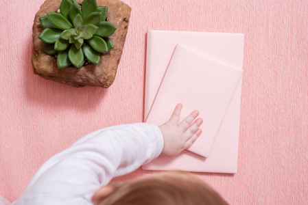 小婴儿的手。 一个可爱的孩子。 粉红色笔记本仙人掌多汁的粉红色背景。 最小的风格。 模仿瓦伦丁。 好奇淘气的孩子