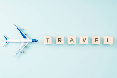 玩具飞机和木制立方体的顶部视图，蓝色背景上有旅行字母