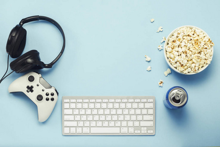 键盘和锡罐与饮料能量，喝一碗爆米花，游戏本和耳机在蓝色背景。 电脑游戏娱乐游戏休闲的概念。 平躺式顶部视图