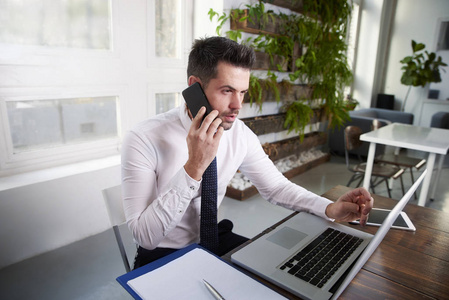 思考金融助理商人在他的手机上说话，在办公室里用笔记本电脑工作。