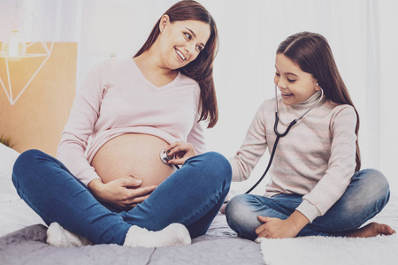 兴奋的女孩听婴儿在母亲肚子里的心跳