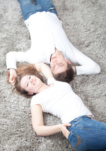 幸福的年轻情侣躺在灰色蓬松的地毯上