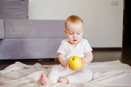 一个可爱的小孩的肖像, 一个黄色的苹果, 坐在地板上。抱着水果的女婴9个月大